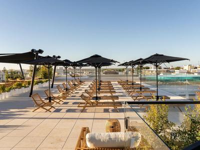 Otwarty taras na dachu z leżakami i parasolami obok basenu pod czystym niebem.