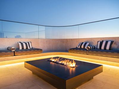 Nowoczesny salon na zewnątrz z wbudowanym paleniskiem i poduszkami o zachodzie słońca.