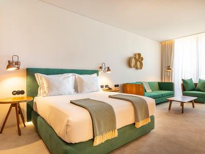 Nowoczesny pokój hotelowy z łóżkiem podwójnym, zieloną sofą i jasnym minimalistycznym wystrojem