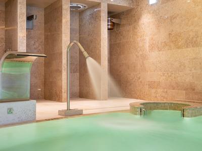 Nowoczesny basen kryty z dyszami wodnymi i beżowymi ścianami z kamienia naturalnego