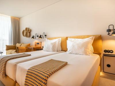 Jasny pokój hotelowy z dwoma pojedynczymi łóżkami, stolikiem nocnym i miejscem do siedzenia.