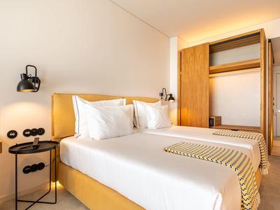 Nowoczesny pokój hotelowy z podwójnym łóżkiem, otwartą szafą i minimalistycznym designem.