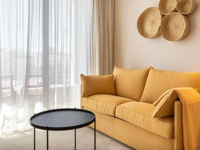 Przytulny salon z żółtą sofą, czarnym stolikiem i dekoracją ścienną z plecionych koszy.