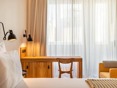 Jasny pokój hotelowy z dużym oknem, drewnianymi meblami i przytulnym łóżkiem