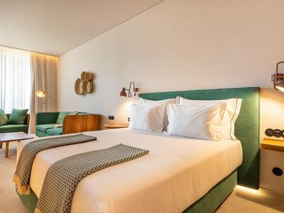 Nowoczesny pokój hotelowy z podwójnym łóżkiem, fotelami i ciepłym oświetleniem.