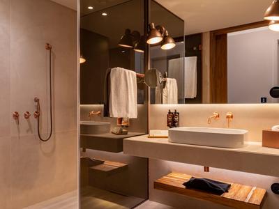 Nowoczesna łazienka z umywalką, lustrem, ręcznikami i prysznicem w brązowych tonach.