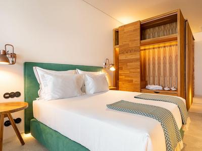 Nowoczesny pokój hotelowy z dużym łóżkiem, zielonym zagłówkiem i otwartą drewnianą szafą.