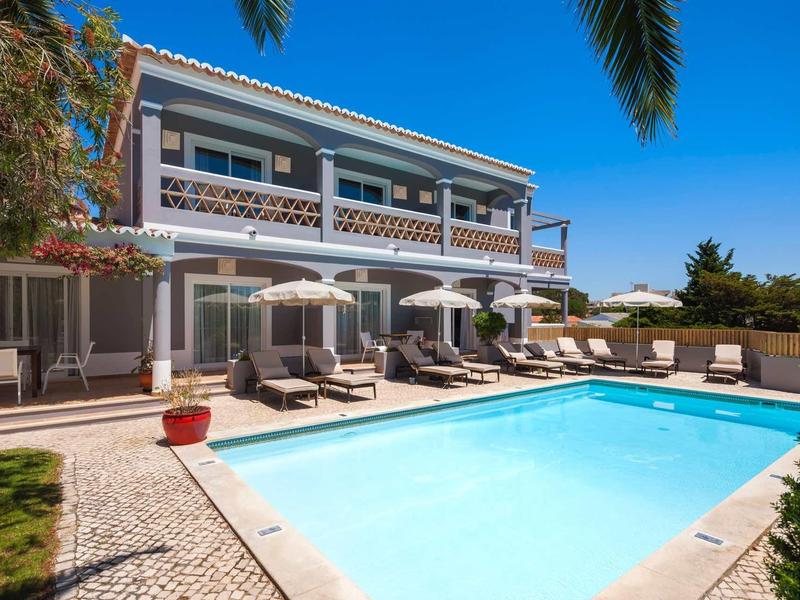 Licht hotel met buitenzwembad, ligstoelen en parasols op een zonnige dag.