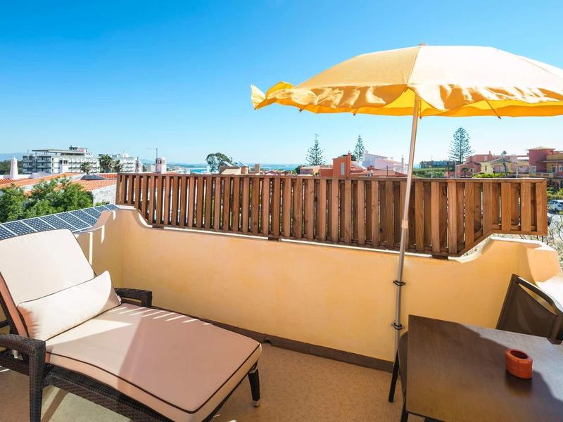 Zonnig balkon met ligstoel, gele parasol en uitzicht op stad en zee.