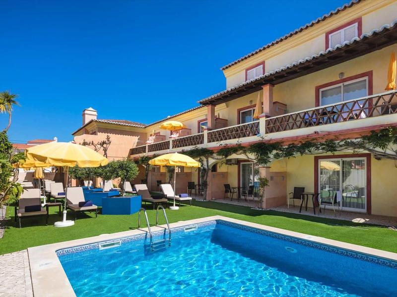 Hotel met een zwembad, ligstoelen en parasols bij zonnig weer.
