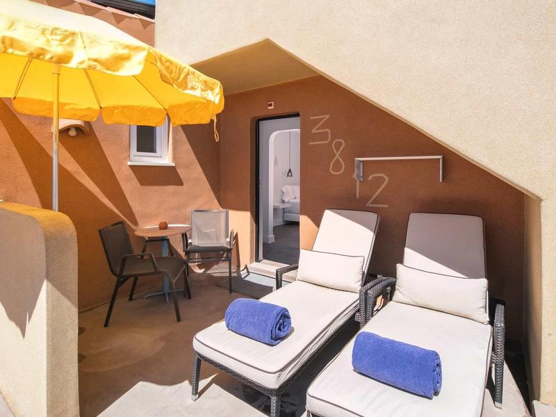 Terras met twee ligstoelen, blauwe handdoeken en een gele parasol bij hotelkamer.