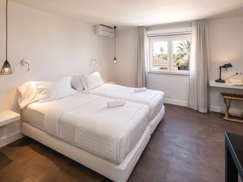 Lichte hotelkamer met twee eenpersoonsbedden, witte muren en een groot raam met gordijnen.