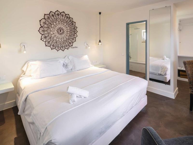 Moderne hotelkamer met groot bed, wit beddengoed en decoratief wandpatroon.