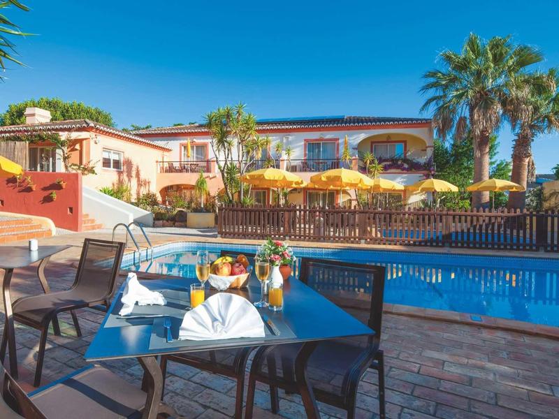 Hotelterras met tafels, parasols en zwembad onder een heldere hemel.