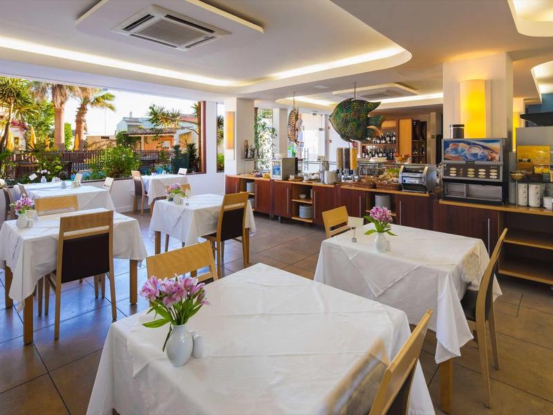 Lichte ontbijtruimte met witte tafelkleden en bloemen, met uitzicht op de tuin.