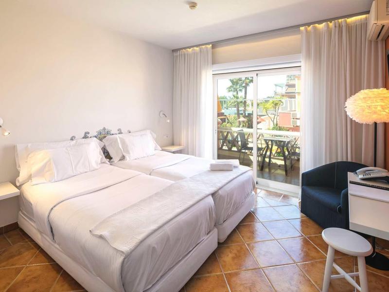 Heldere hotelkamer met twee eenpersoonsbedden, balkondeur en balkon met planten