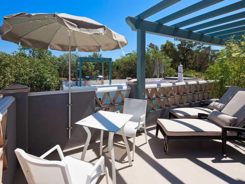 Terras met parasol, tafel, stoelen en ligbedden onder een blauwe lucht.