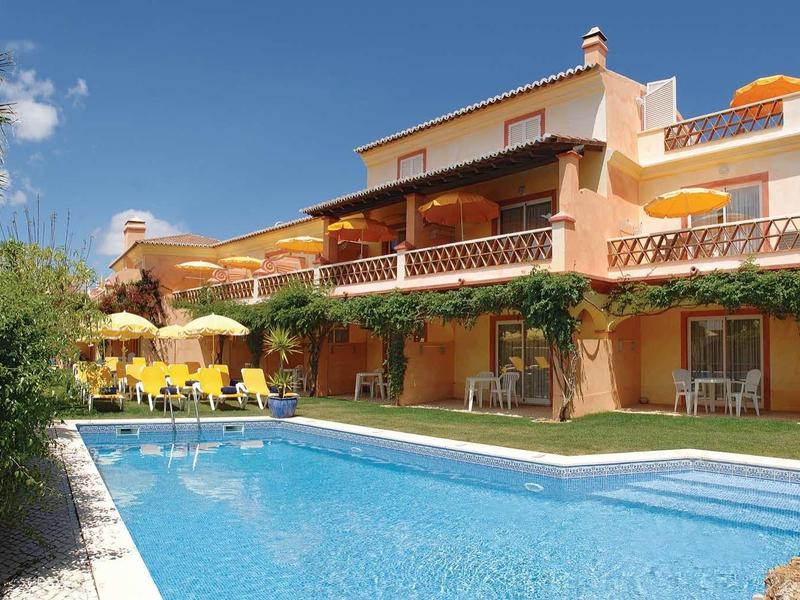 Groot vakantiehuis met zwembad en parasols onder blauwe lucht