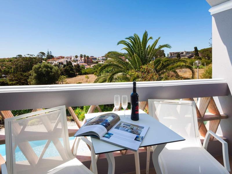 Balkon met twee stoelen, tafel, wijnfles en open boek met uitzicht op het landschap.