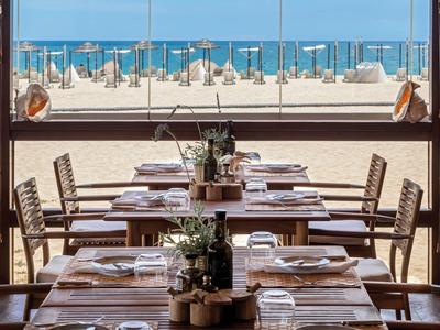 Uitzicht op gedekte tafels in een restaurant met uitzicht op een zandstrand en de zee.