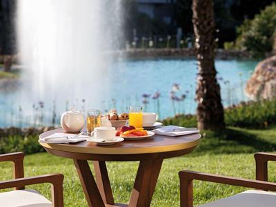 Kleine ronde houten tafel met ontbijt bij fontein en meer op de achtergrond.