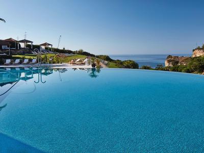 Infinity zwembad met uitzicht op zee en ligstoelen onder parasols.