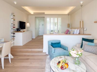 Lichte hotelkamer met zithoek, bed, bureau en moderne inrichting in neutrale tinten.