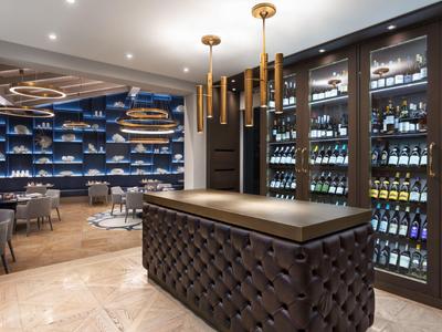 Moderne hotelbar met donkere toonbank, wijnkoelers en elegante zithoek op de achtergrond.