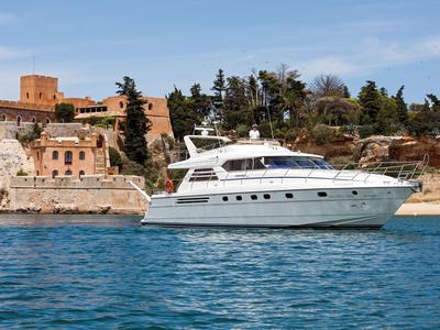 Luxe wit jacht bij de kust met historische gebouwen en bomen op de achtergrond.