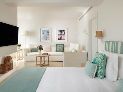 Lichte hotelkamer met een comfortabel tweepersoonsbed, bank en minimalistische inrichting in rustgevende kleuren.