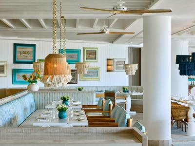 Licht, modern restaurant met houten tafels, blauwe banken en decoratieve schilderijen aan de muren.