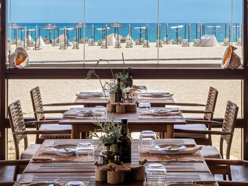 Uitzicht op gedekte tafels in een restaurant met uitzicht op een zandstrand en de zee.