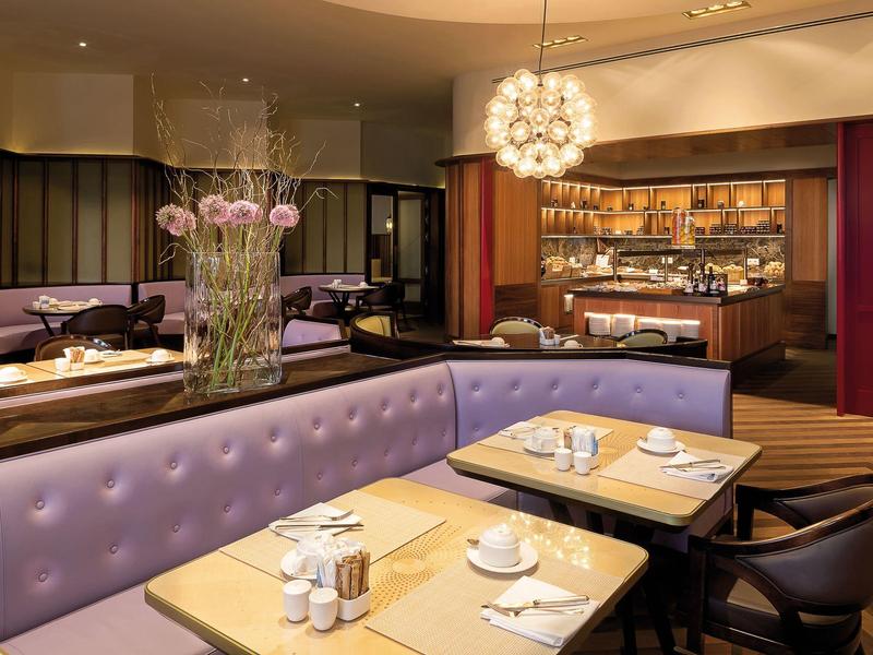 Modern hotelrestaurant met paarse banken en elegant gedekte tafels.