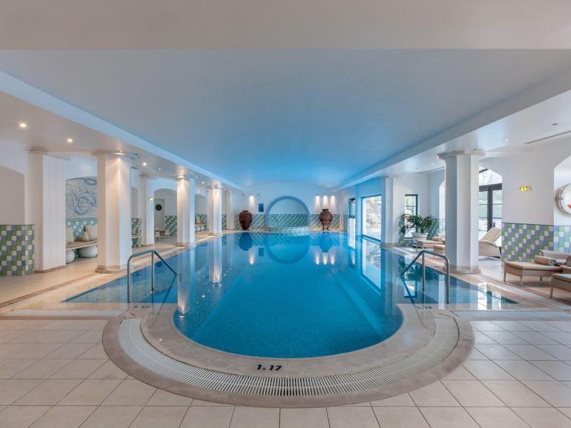 Binnenzwembad in een modern wellnesshotel met ronde ramen en ligstoelen.