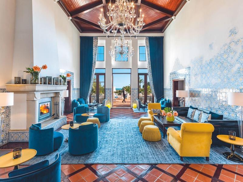 Elegante hotellobby met blauwe fauteuils, gele stoelen, open haard en kroonluchter.