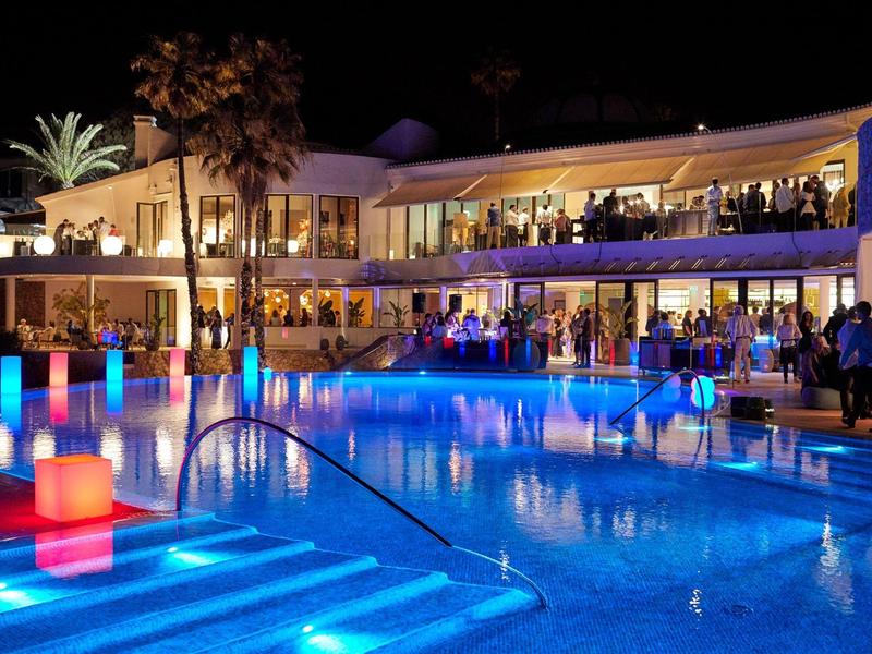 Verlicht hotelzwembad met gasten en kleurrijke lichten 's nachts