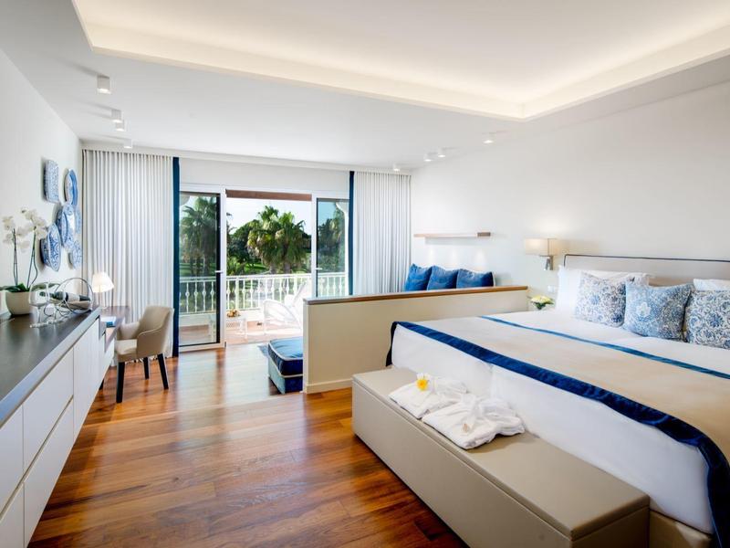 Modern hotelkamer met groot bed, houten vloer en balkon met uitzicht op groen.