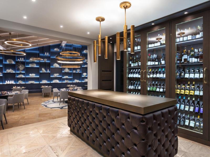 Moderne hotelbar met donkere toonbank, wijnkoelers en elegante zithoek op de achtergrond.