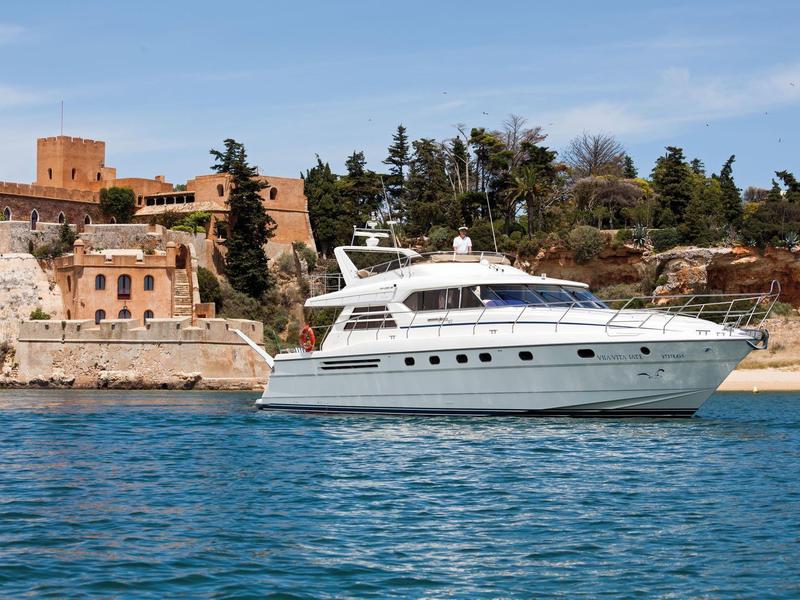 Luxe wit jacht bij de kust met historische gebouwen en bomen op de achtergrond.