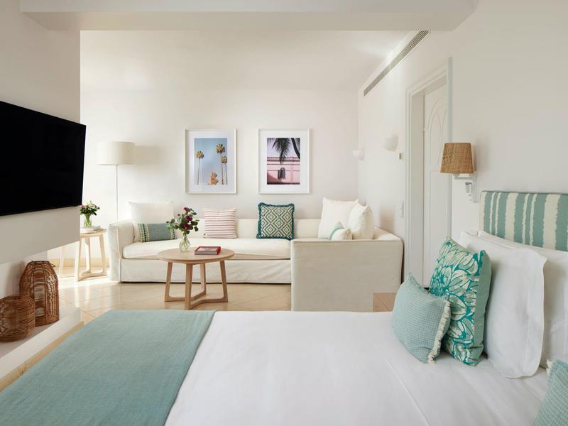 Lichte hotelkamer met een comfortabel tweepersoonsbed, bank en minimalistische inrichting in rustgevende kleuren.