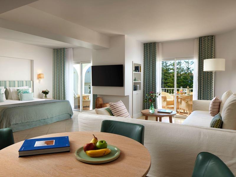 Modern ingerichte hotelkamer met zithoek, bed en terras met uitzicht op groen.