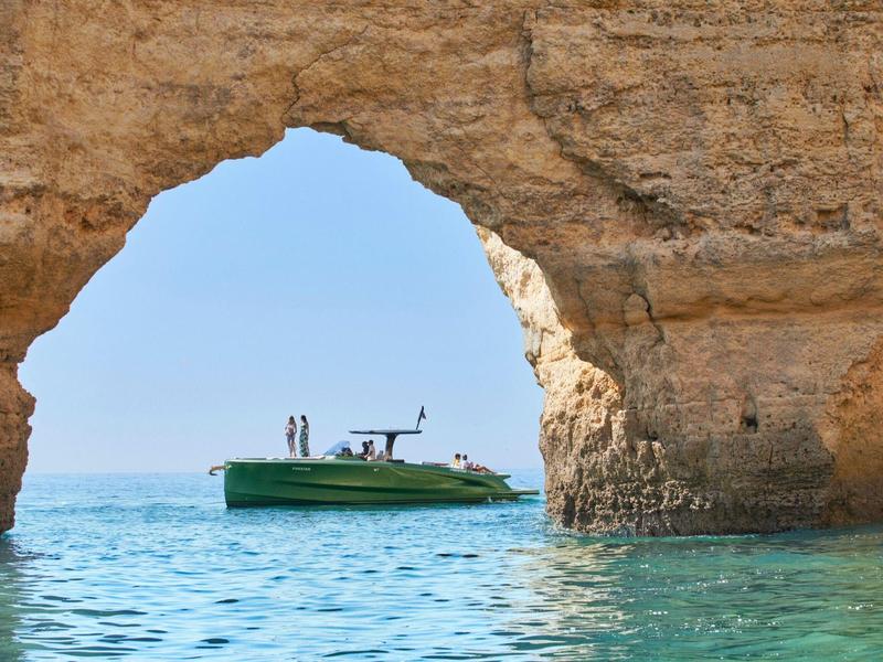 Boot vaart door natuurlijke rotsboog bij zonnige dag met heldere lucht en kalme zee.
