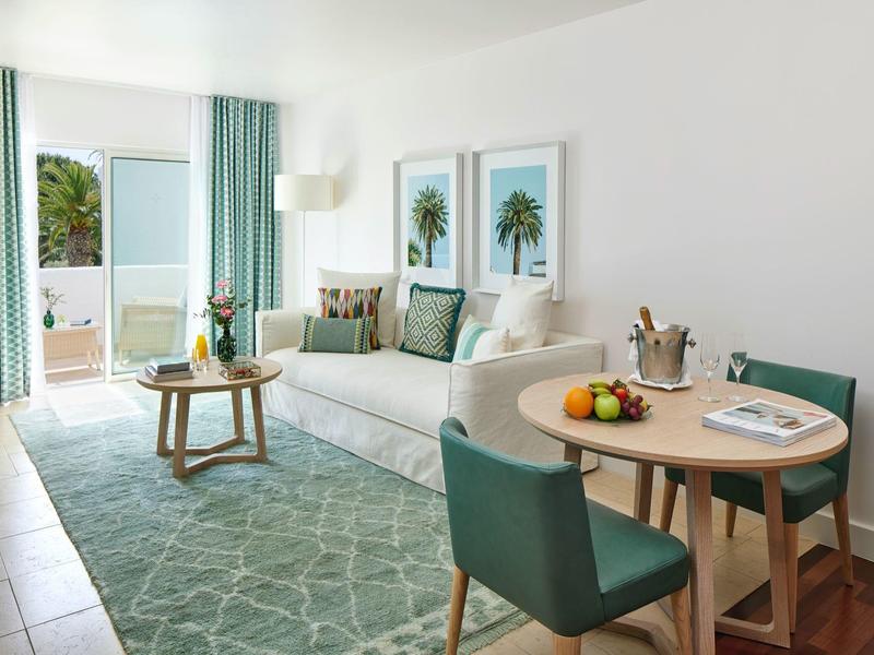 Lichte woonkamer met bank, tapijt, eettafel en balkon met uitzicht op zee.