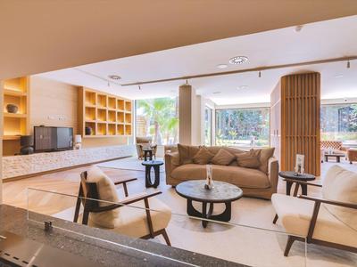 Helles Wohnzimmer mit beiger Couch, Holzregalen, zwei Sesseln und großem Fenster mit grünem Ausblick.