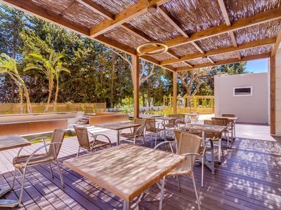 Überdachte Terrasse mit Holz- und Metallmöbeln, umgeben von Bäumen und sonnigem Wetter.