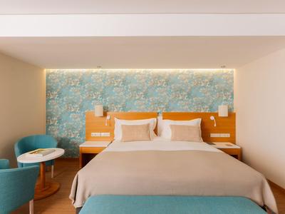 Modernes Hotelzimmer mit Doppelbett, blauer Akzentwand und zwei blauen Sesseln mit Tisch.