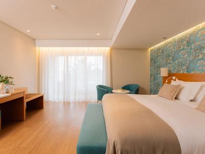 Modern eingerichtetes Hotelzimmer mit großem Bett, Holzfußboden und Sitzbereich.