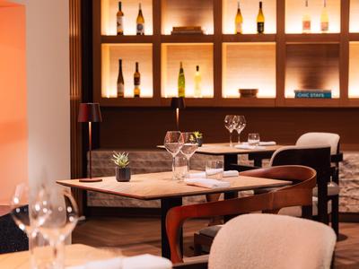 Elegantes Restaurant mit beleuchteten Flaschenregalen und gedeckten Tischen mit Gläsern.