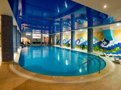Innen-Pool mit blauem Wasser, bunten Mosaikwänden und weißen Liegestühlen am Rand.