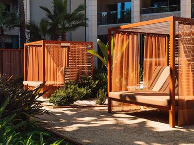 Zwei hölzerne überdachte Liegen neben einem Pool mit grünen Pflanzen dazwischen.